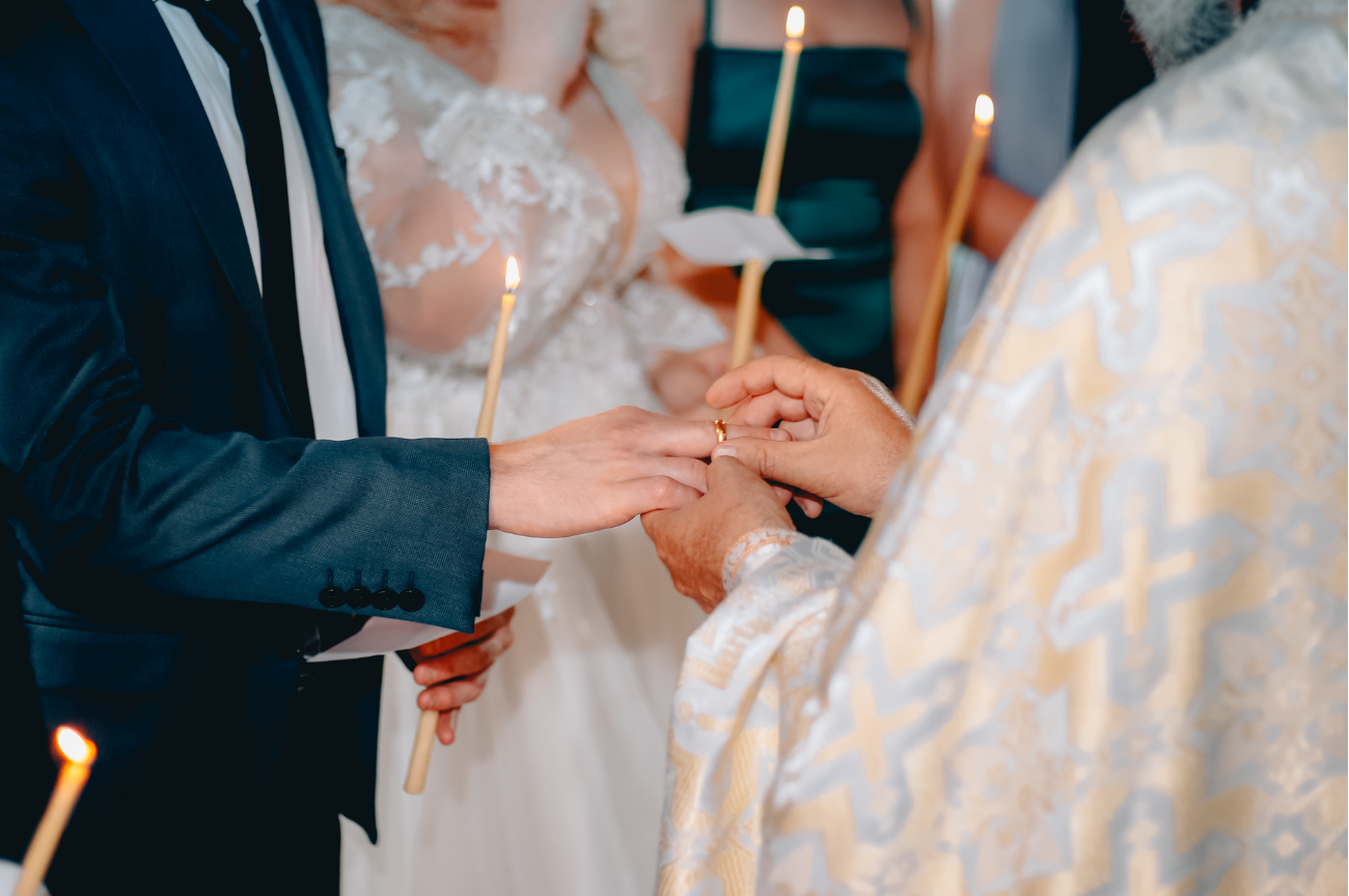 Un prêtre passe l'alliance au marié pendant la cérémonie religieuse, entouré de cierges allumés